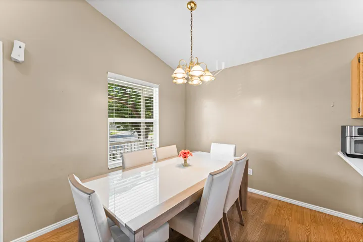 Dining area featuring a vaulted ceiling, wood-finish flooring, and a window with blinds