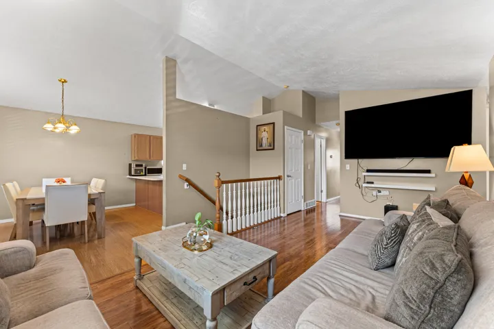 Open-concept living area featuring vaulted ceilings, wood-finish flooring, a built-in entertainment wall, and a dining area with a brass chandelier