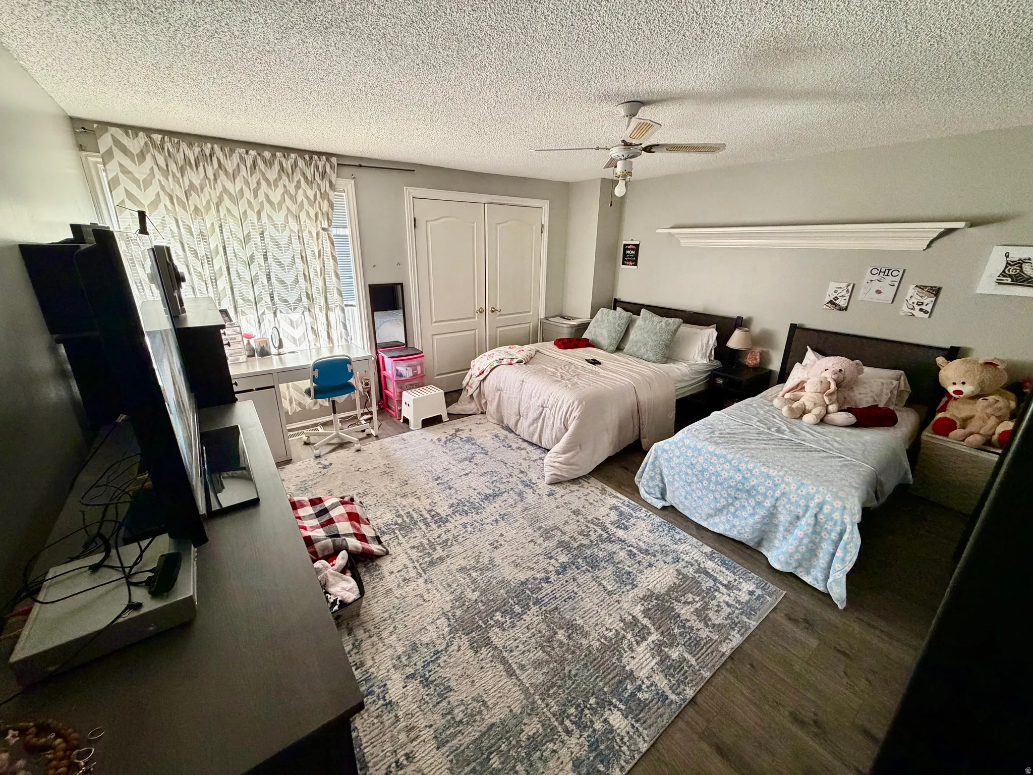 Spacious room featuring wood-finish flooring, a contemporary ceiling fan, and ample natural light from a window with chevron-patterned drapes