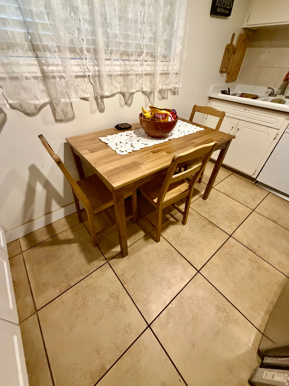 Kitchen area featuring light-toned tile flooring, white cabinetry, and a window with blinds