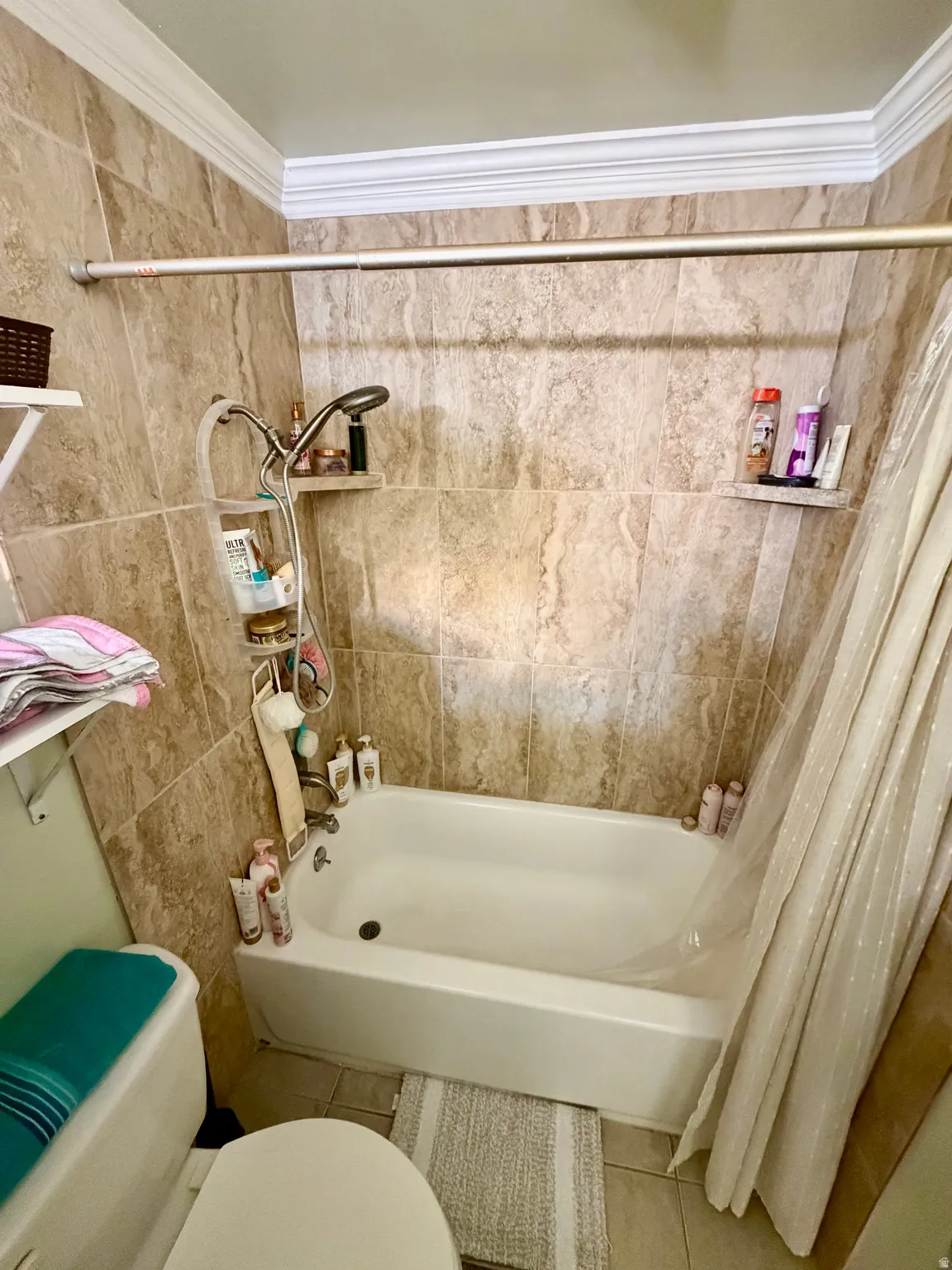 Bathtub with surrounding tile walls, crown molding, and a wall-mounted shower head