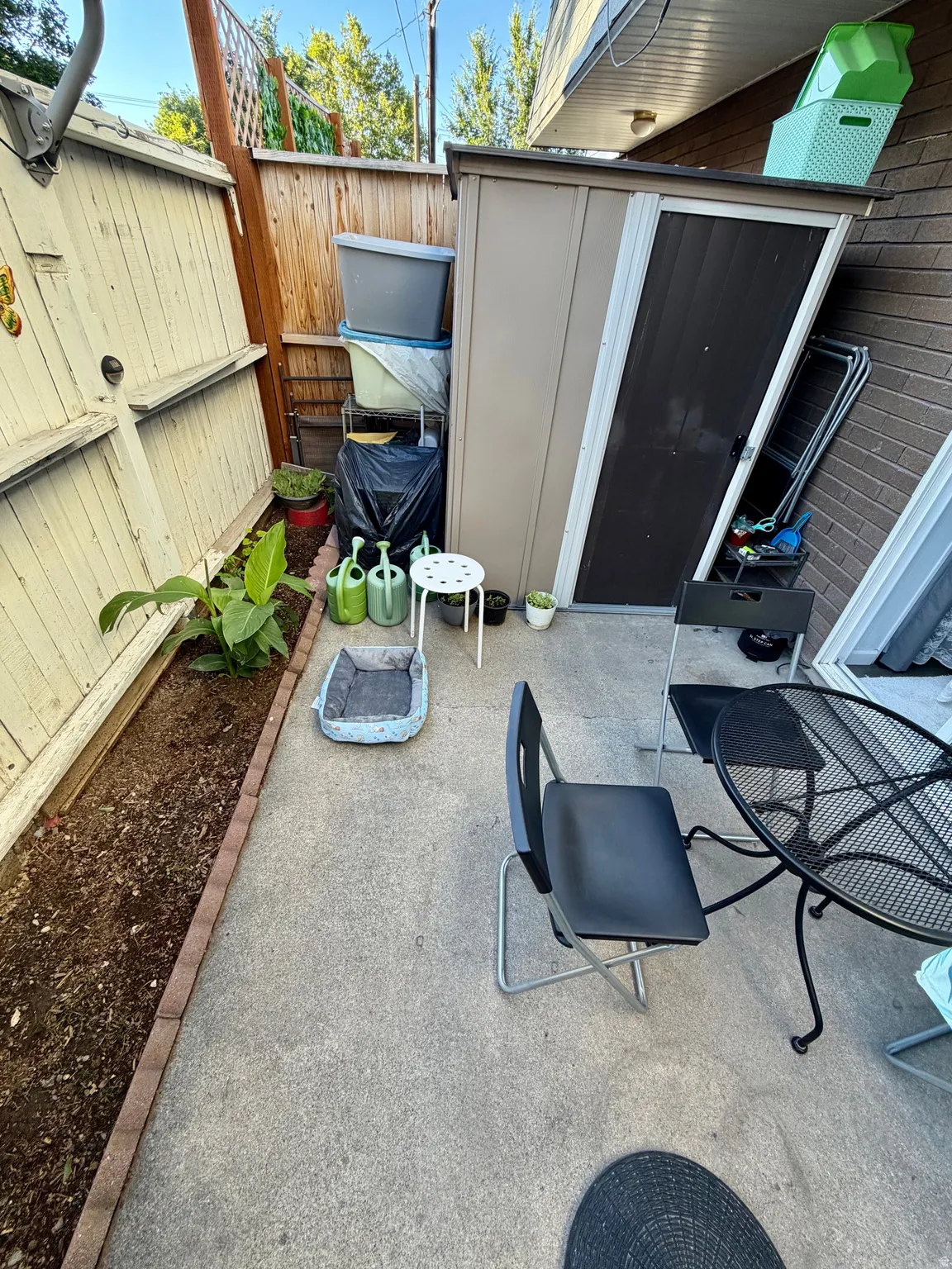 Paved outdoor area featuring a tan storage shed, brick wall, and wood fencing
