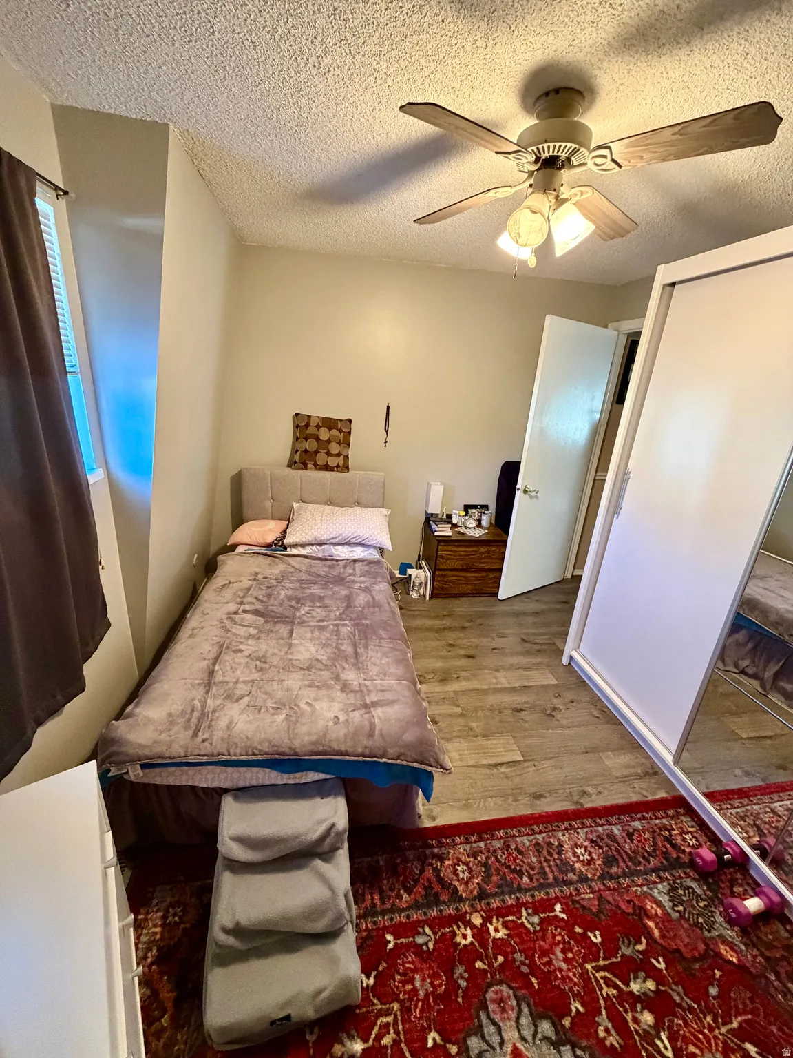 Bedroom featuring wood-finish flooring, a ceiling fan with integrated lighting, and a mirrored sliding closet door