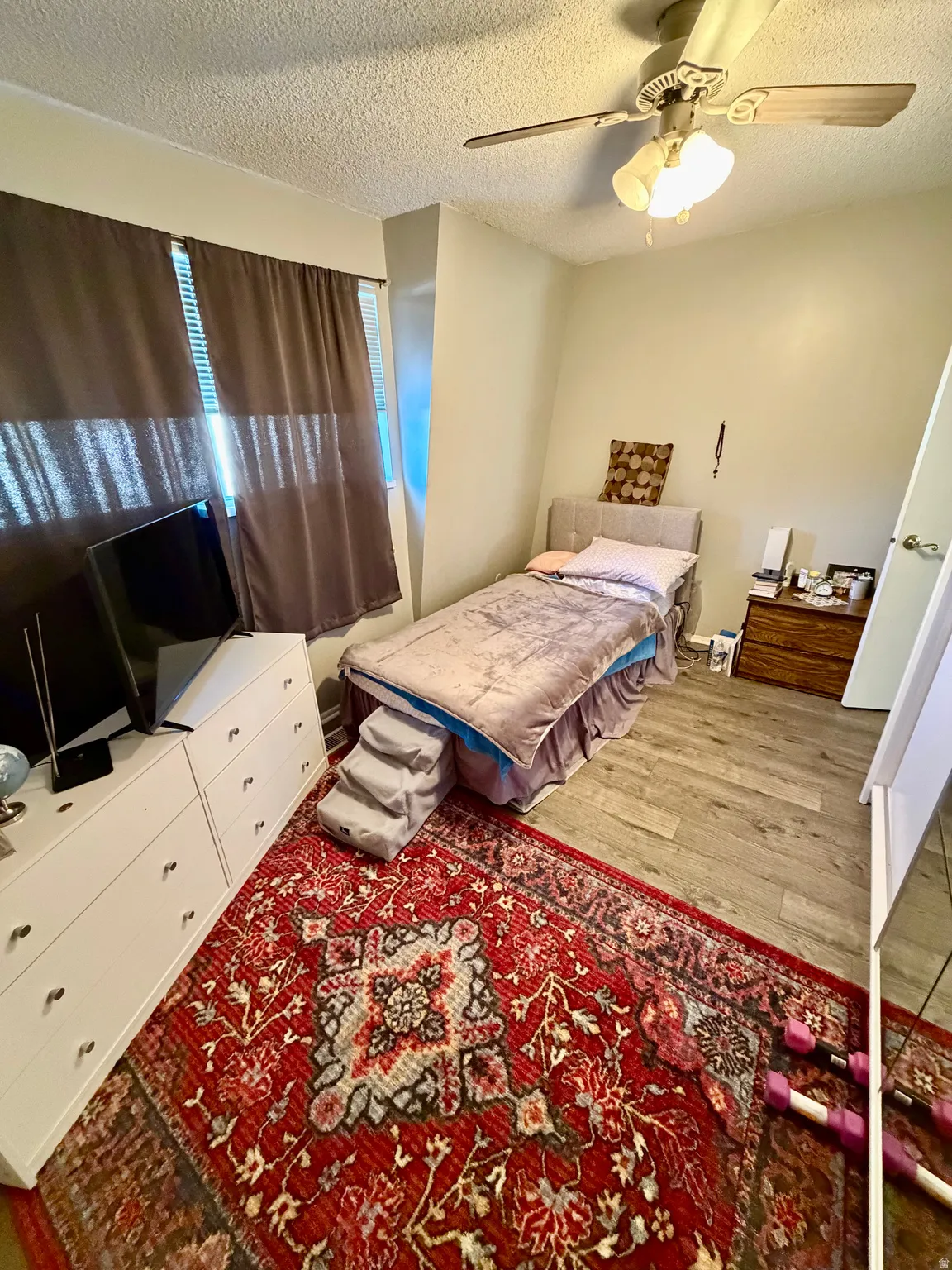 Bedroom featuring wood-finish flooring, a ceiling fan with integrated lighting, and window treatments