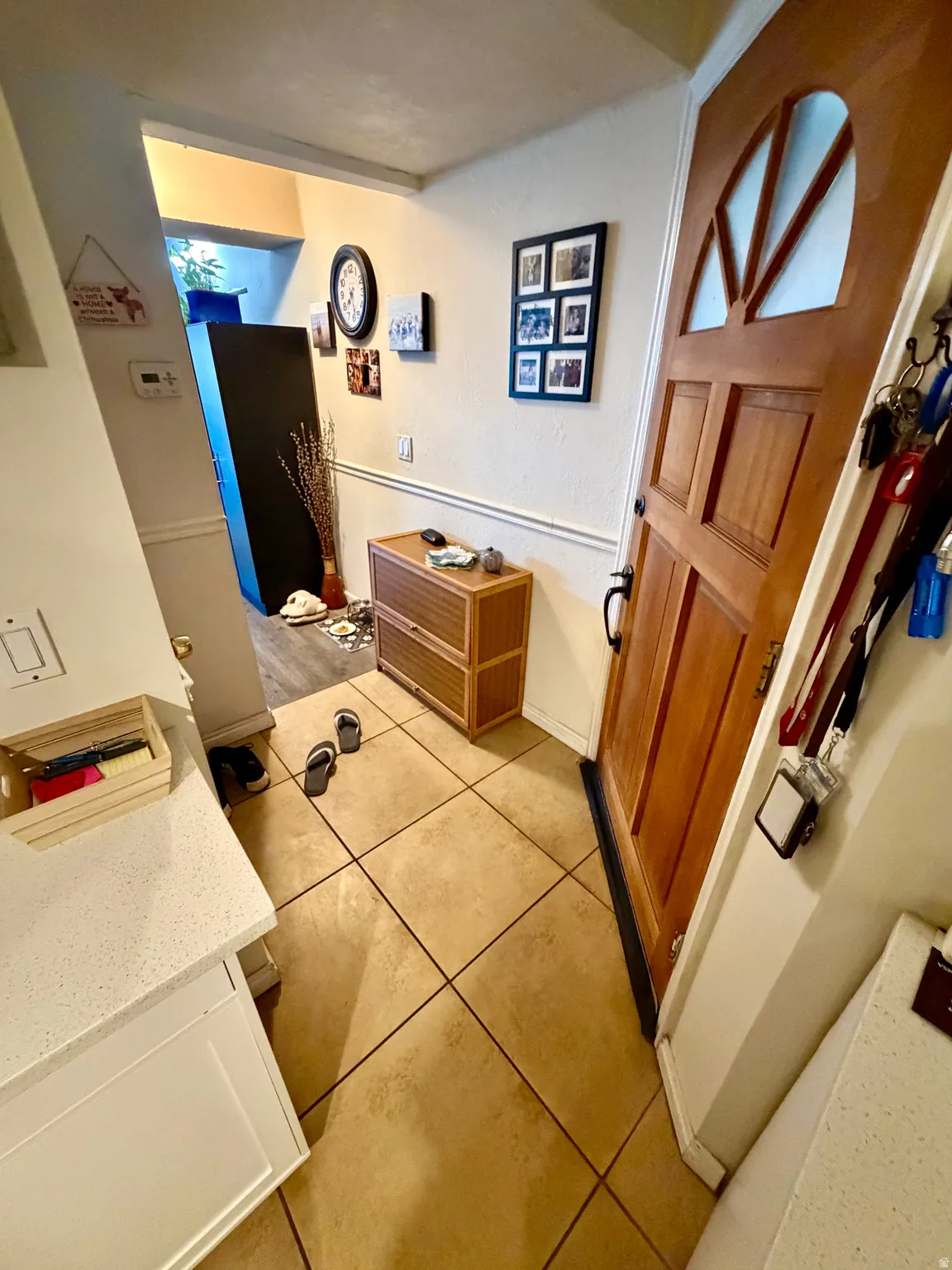 Entryway featuring warm-toned tile flooring, light wood-paneled door with decorative glass inserts, and a built-in countertop with white cabinetry