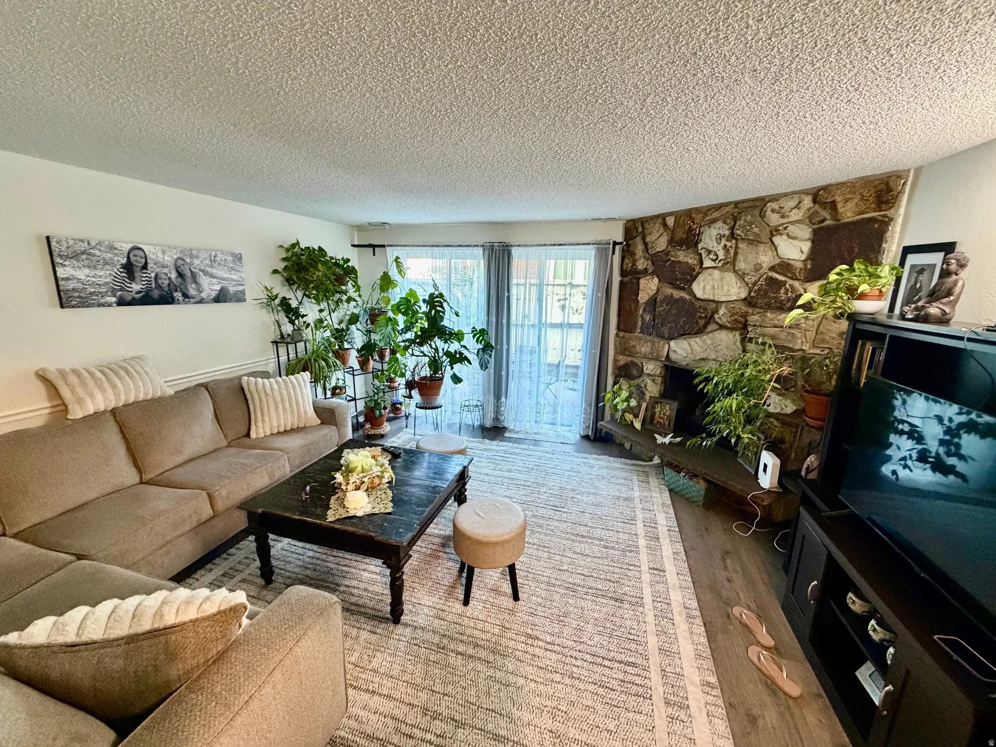 Living area featuring a floor-to-ceiling stone fireplace, dual sliding glass doors, wood-finish flooring, and crown molding