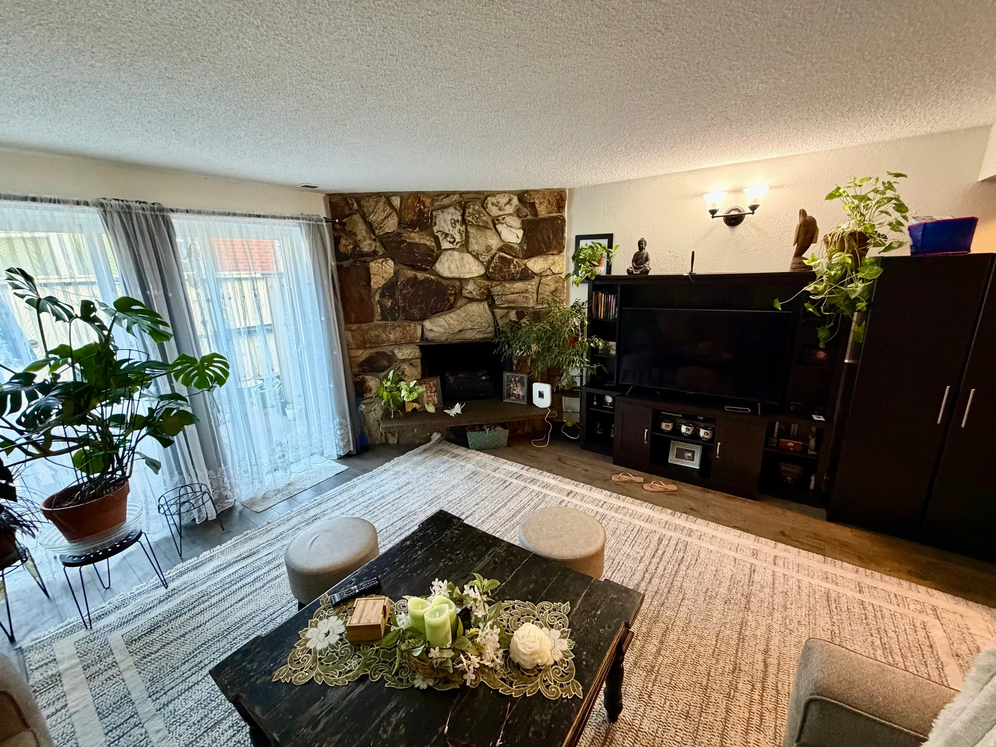 Living area featuring a floor-to-ceiling stone fireplace, wood-finish flooring, and a large window with sheer drapes