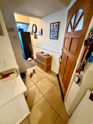 Entryway featuring warm-toned tile flooring, light wood-paneled door with decorative glass inserts, and a built-in countertop with white cabinetry