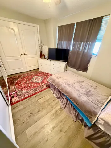 Wood-finish flooring throughout, featuring a double-door closet with arch paneling, a ceiling fan, and window with blinds