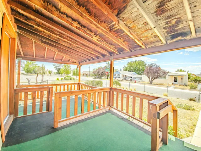 Covered front porch featuring natural wood ceiling, wood railing, and green outdoor carpeting