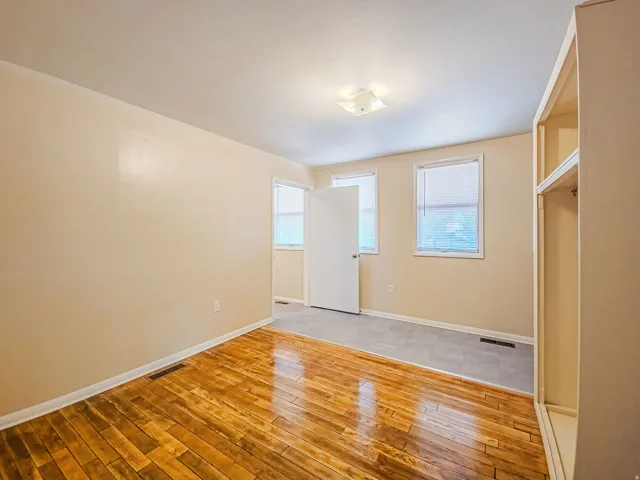 Interior room featuring wood-finish flooring, two windows with blinds, a ceiling-mounted light fixture, and a built-in shelving unit