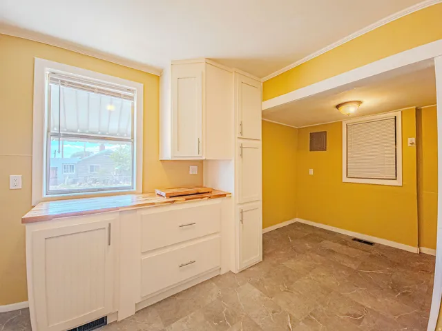 Kitchen area featuring white cabinetry with brushed nickel hardware, wood-finish countertops, and grey-toned tile flooring
