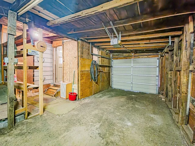Interior garage space featuring a roll-up garage door, exposed wood beam ceiling, and concrete flooring