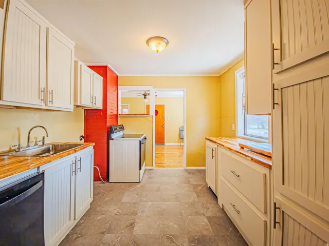Kitchen featuring light-toned cabinetry with T-bar pulls, butcher block style countertops, and a stainless steel double basin sink