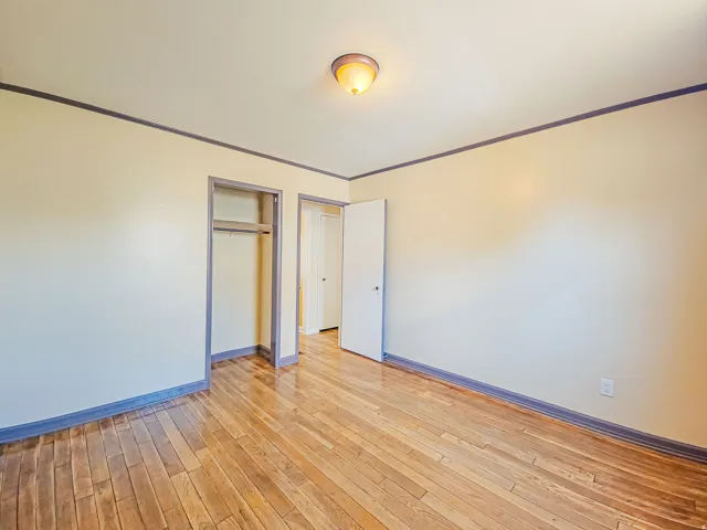 Room featuring wood-finish flooring, light-toned walls with contrasting trim, a flush-mount ceiling light fixture, and an open closet space with a clothes rod
