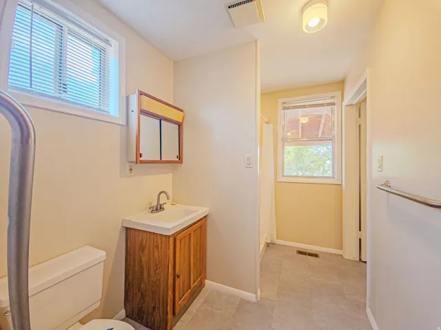 Bathroom featuring a wood-finish vanity with an integrated sink, mirrored medicine cabinet, and a window with blinds
