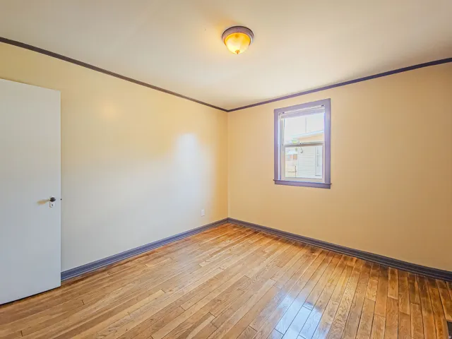 Hardwood flooring throughout featuring a neutral wall color, trim detailing, and a single window