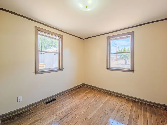 Room featuring wood-finish flooring, two window openings, neutral-toned walls, contrasting trim, and a ceiling-mounted light fixture
