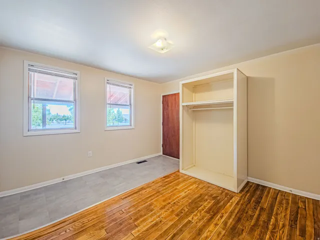 Interior room featuring wood-finish flooring, a built-in wardrobe with hanging rod and shelving, and two windows