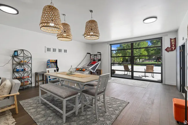 Spacious recreation room featuring large floor-to-ceiling glass panel doors, dark wood-finish flooring, recessed lighting, and three woven pendant light fixtures