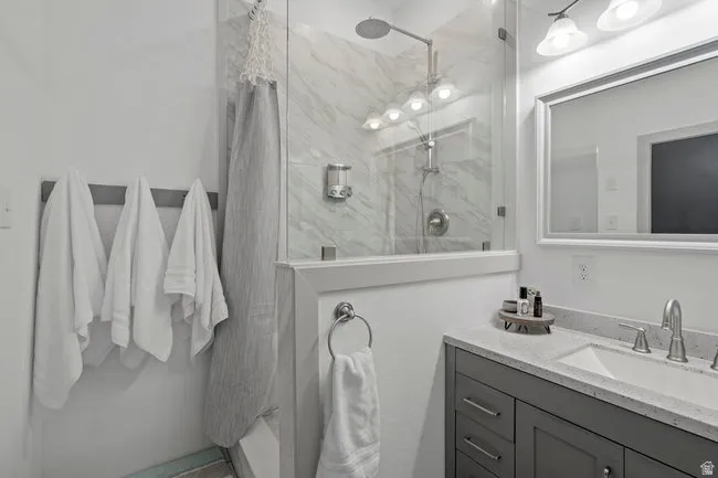 Modern bathroom featuring a glass-enclosed shower with marble-look tile, a rain shower head, a single vanity with a light gray countertop, and a framed mirror