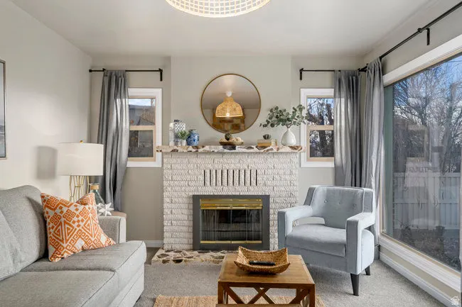 Living area featuring a white brick fireplace with a brass-trimmed insert, flanked by two windows
