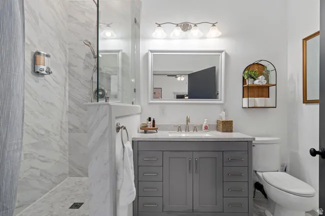 Bathroom featuring a walk-in shower with marble-look wall tiling, a glass shower partition, a gray vanity with a quartz-style countertop, and a contemporary mirror