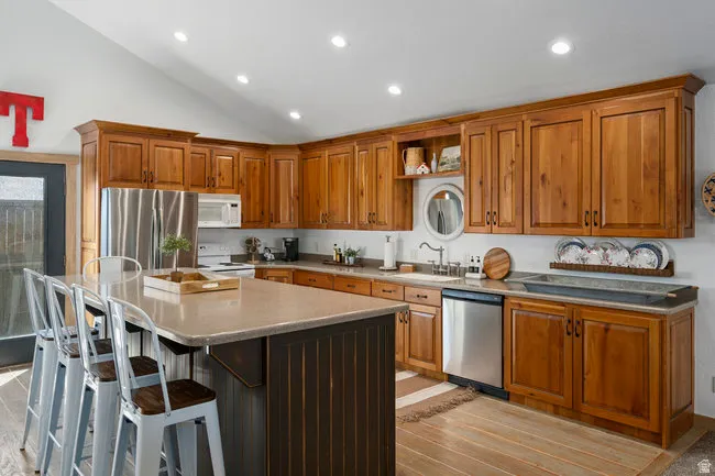 Spacious kitchen featuring extensive wood cabinetry, stainless steel appliances, a large island with counter seating, light-toned countertops, and recessed lighting