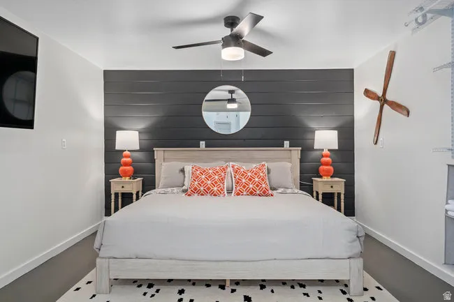 Bedroom featuring a dark accent wall with horizontal paneling, a ceiling fan with integrated lighting, a built-in wall-mounted television, and hard-surface flooring