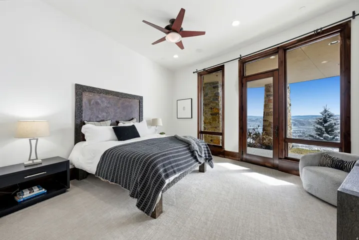 Bedroom featuring a vaulted ceiling with a ceiling fan, wall-to-wall carpeting, and floor-to-ceiling windows with dark wood frames