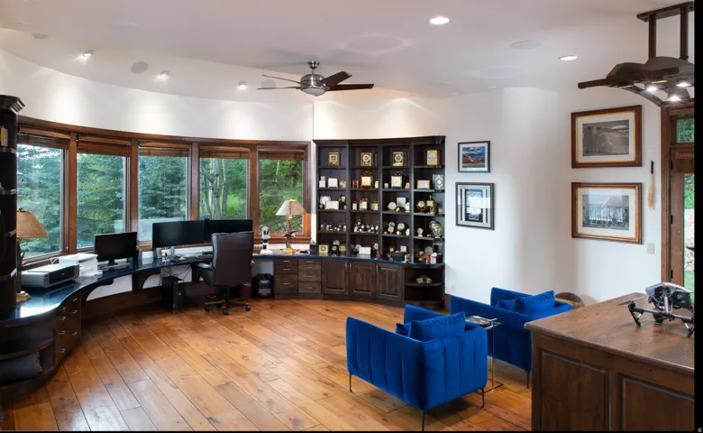 Dedicated office space featuring expansive curved windows, wood-finish flooring, built-in desk cabinetry, recessed lighting, and a ceiling fan