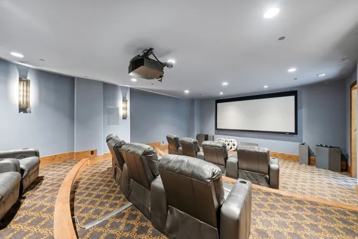 Dedicated home theater featuring a large projection screen, ceiling-mounted projector, patterned carpeting, and recessed lighting