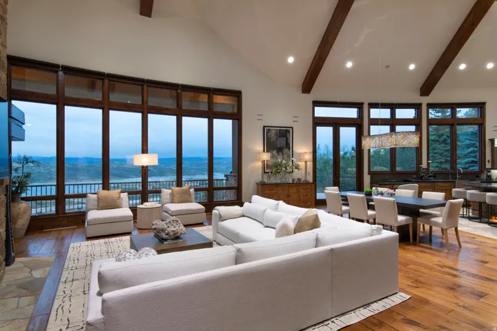 Expansive great room featuring a vaulted ceiling with exposed wood beams, hardwood flooring, and a stone fireplace surround