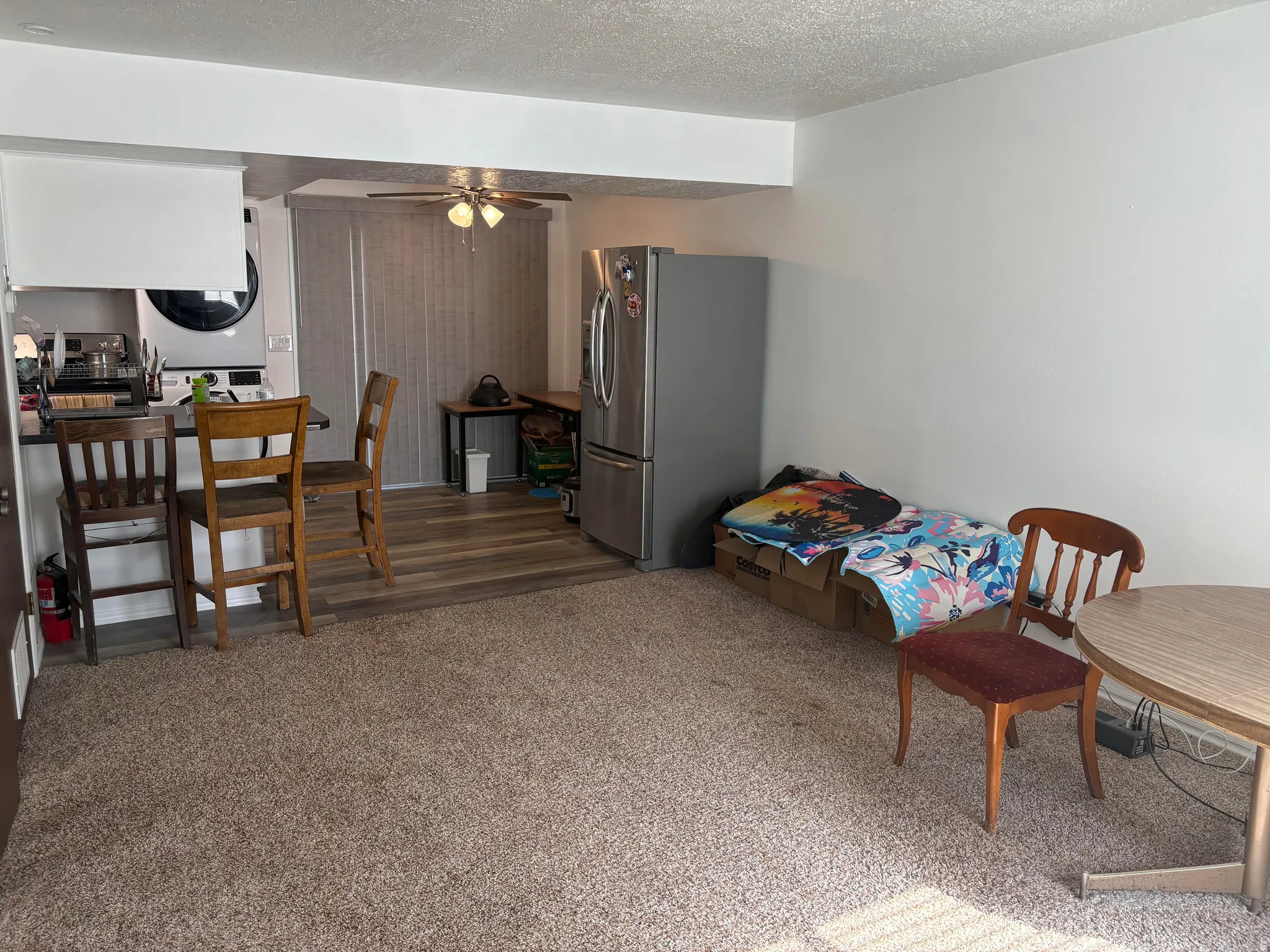 Living area featuring carpet flooring, an open-concept kitchen bar, and a laundry area with stacked appliances
