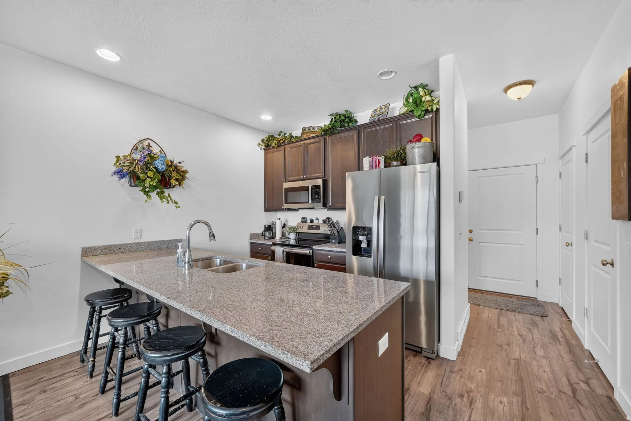 Kitchen featuring a peninsula with double basin sink, dark wood-finish cabinetry, stainless steel appliances, and light-toned countertops