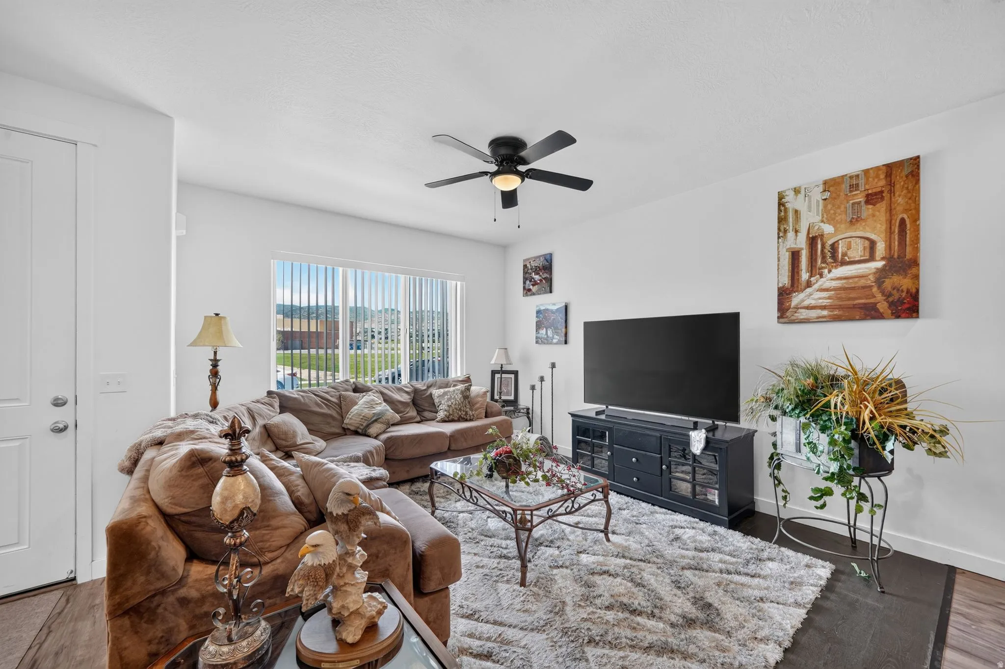Bright interior room featuring a ceiling fan, a large window with vertical blinds, and wood-finish flooring