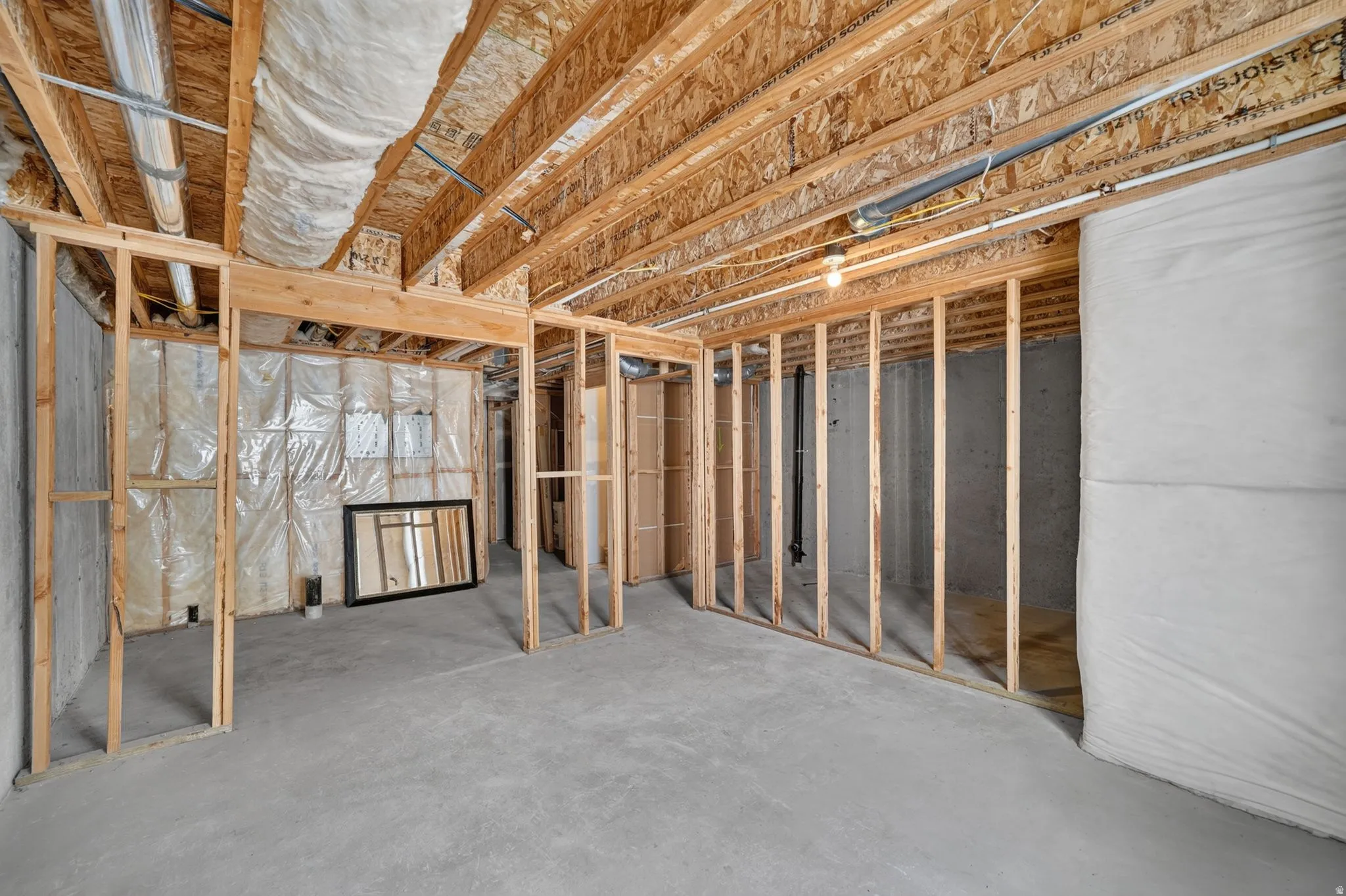 Unfinished basement featuring wood framing, exposed ceiling joists, concrete flooring, and insulated walls