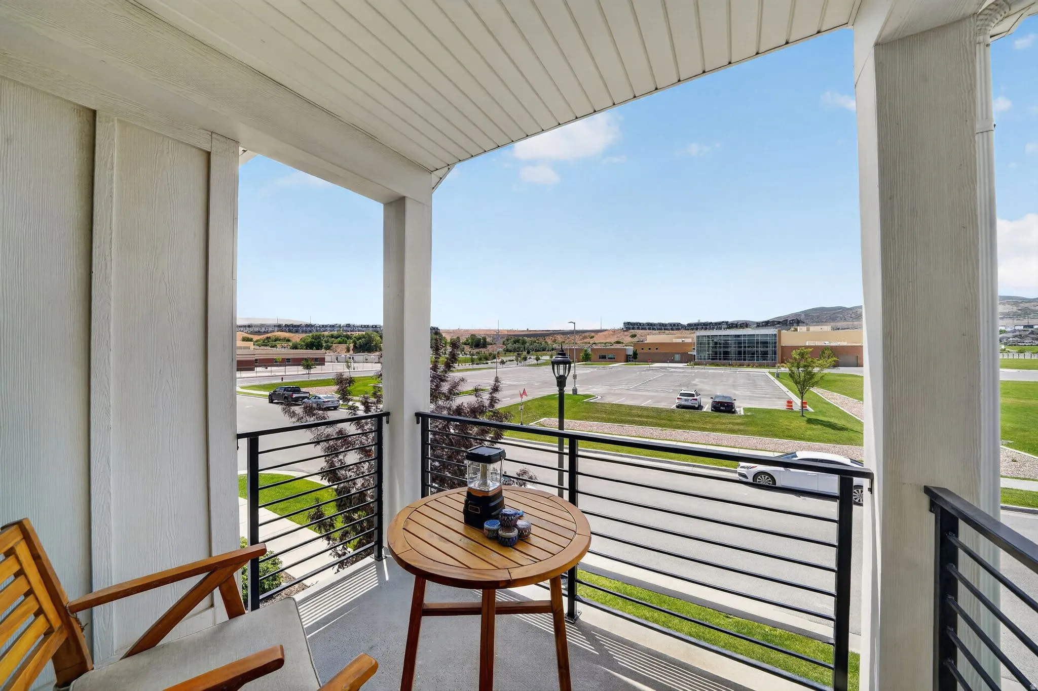 Outdoor balcony featuring white siding, a black horizontal bar railing, and a view of surrounding buildings and open fields
