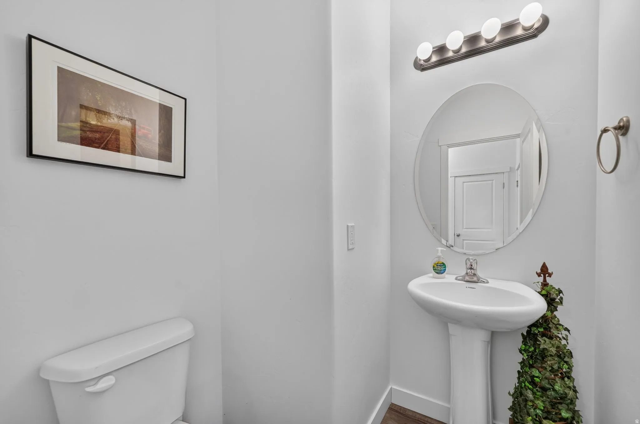 Pedestal sink with a brushed nickel faucet, an oval mirror, and a four-bulb vanity light fixture