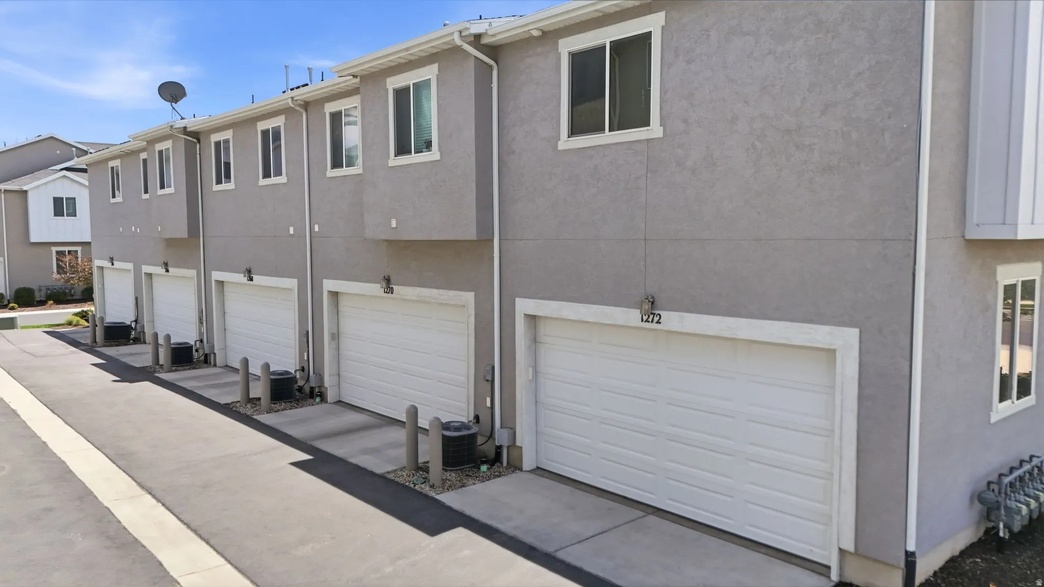 Stucco exterior with multiple white garage doors, white-framed windows, and individual exterior lighting fixtures