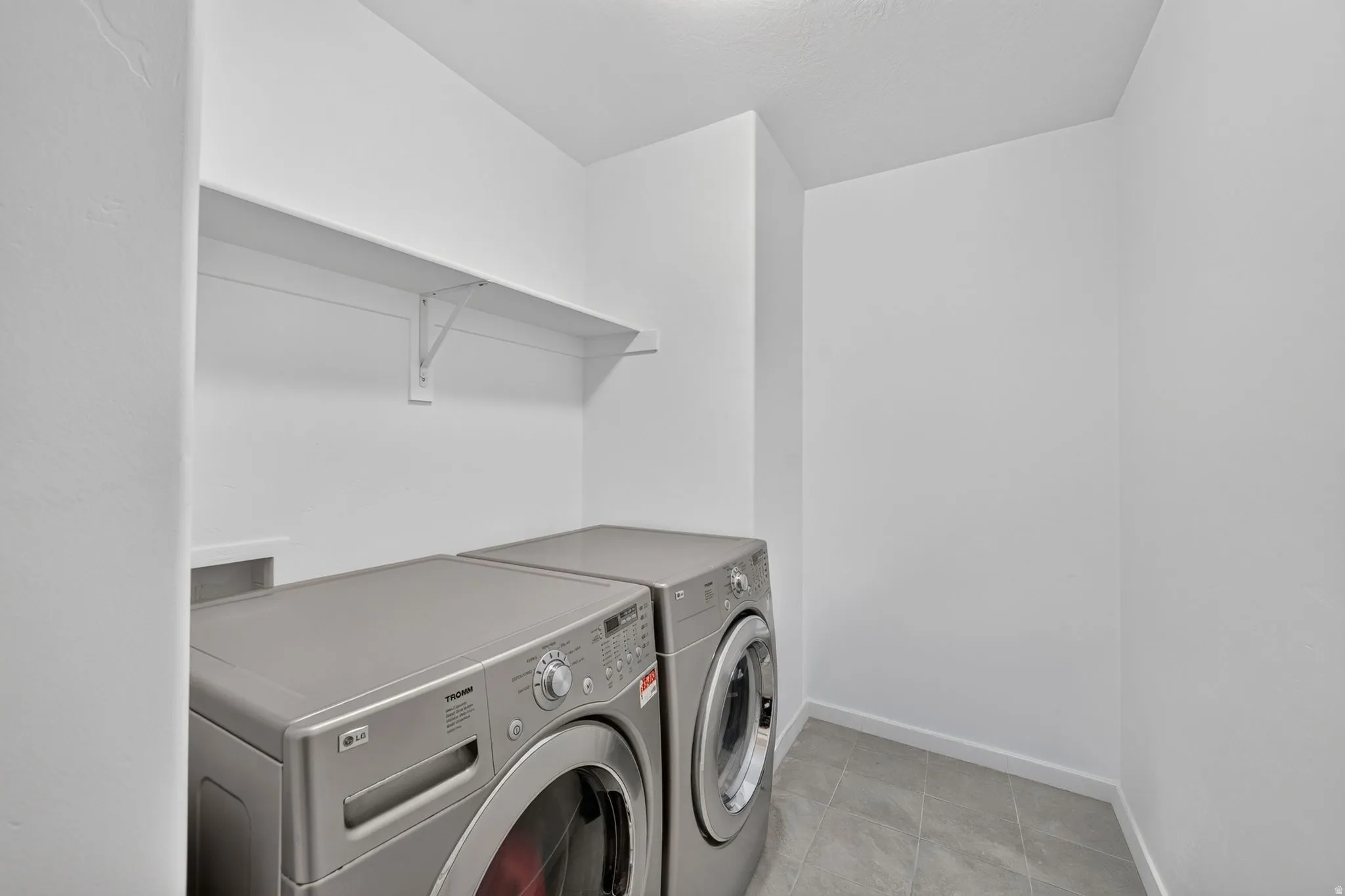 Dedicated laundry area featuring a wall-mounted shelf, light gray floor tiles, and crisp white walls