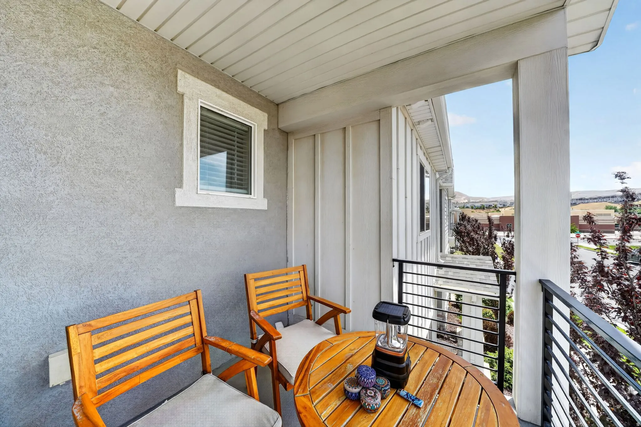 Private exterior balcony featuring a stucco wall, white vinyl window, and modern horizontal metal railing