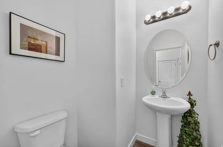 Pedestal sink with a brushed nickel faucet, an oval mirror, and a four-bulb vanity light fixture