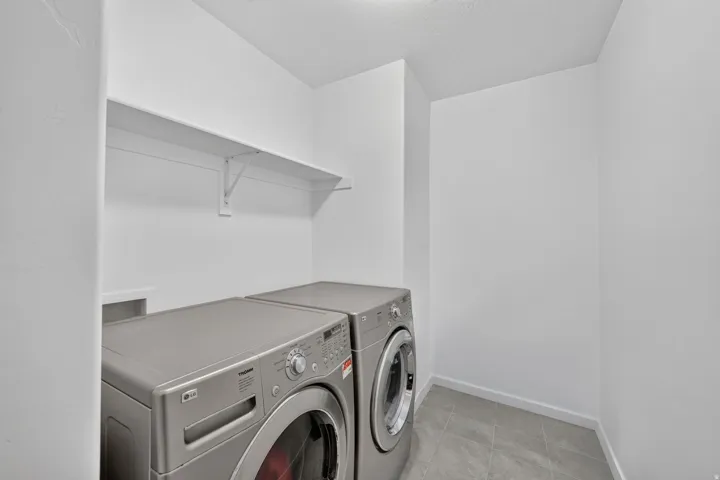 Dedicated laundry area featuring a wall-mounted shelf, light gray floor tiles, and crisp white walls