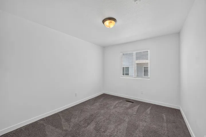 Neutral white walls with a single window, ceiling-mounted light fixture, and dark gray carpeting