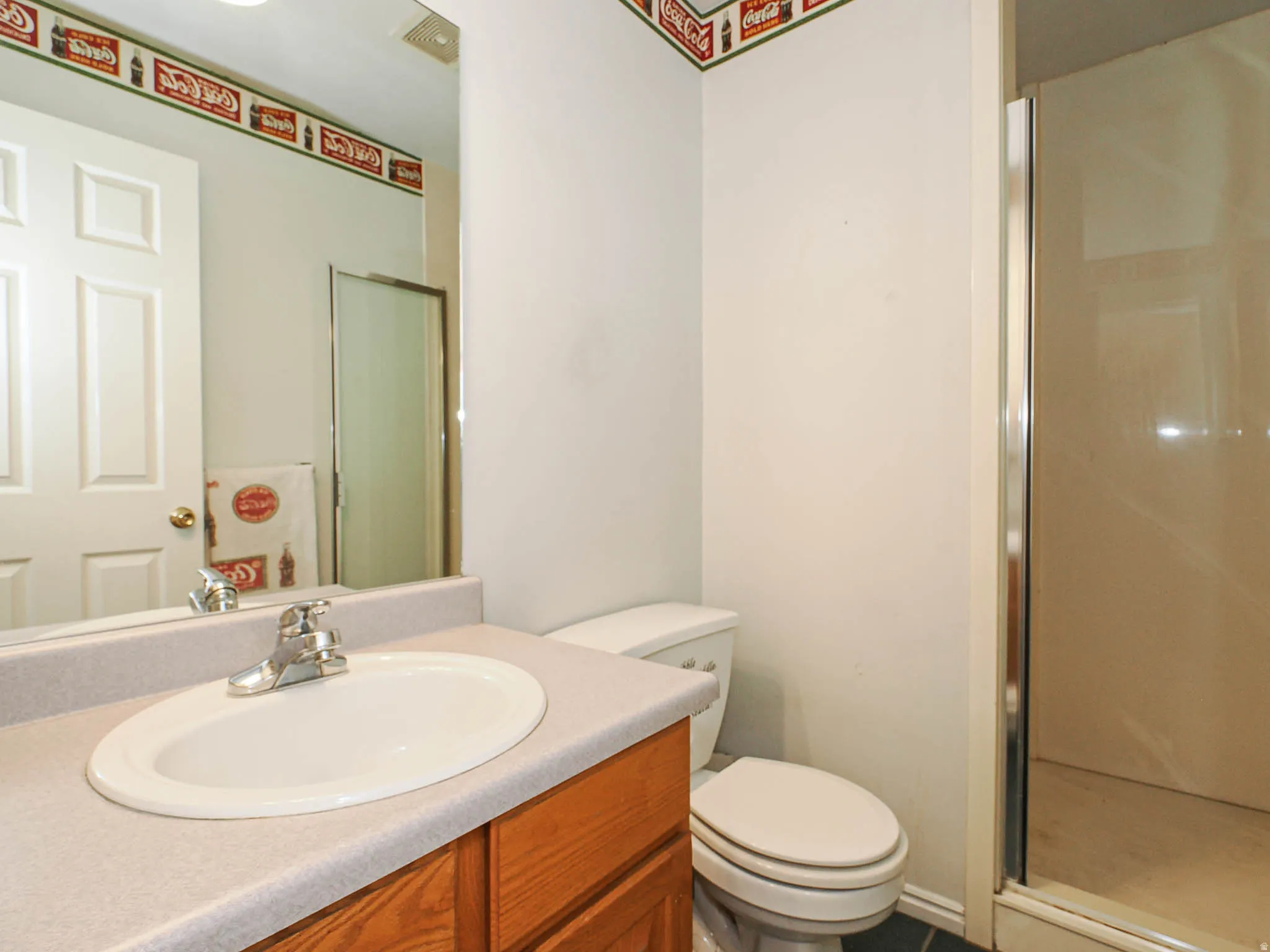 Bathroom featuring a wood vanity with an integrated sink, chrome faucet, wall-mounted mirror, and a standing shower enclosure