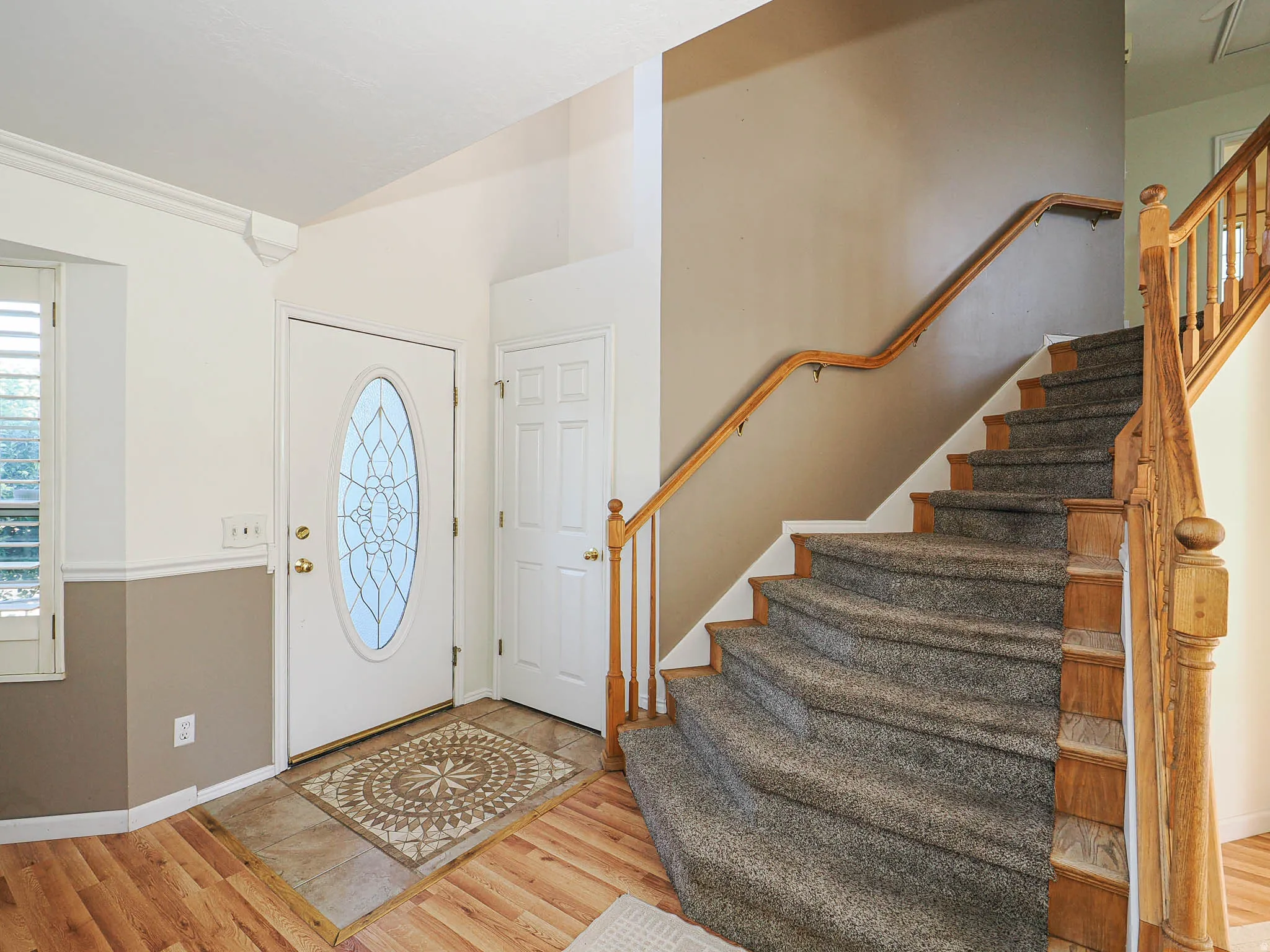 Entryway featuring a decorative oval-paneled front door, wood-finish flooring, and a carpeted staircase with a wood handrail