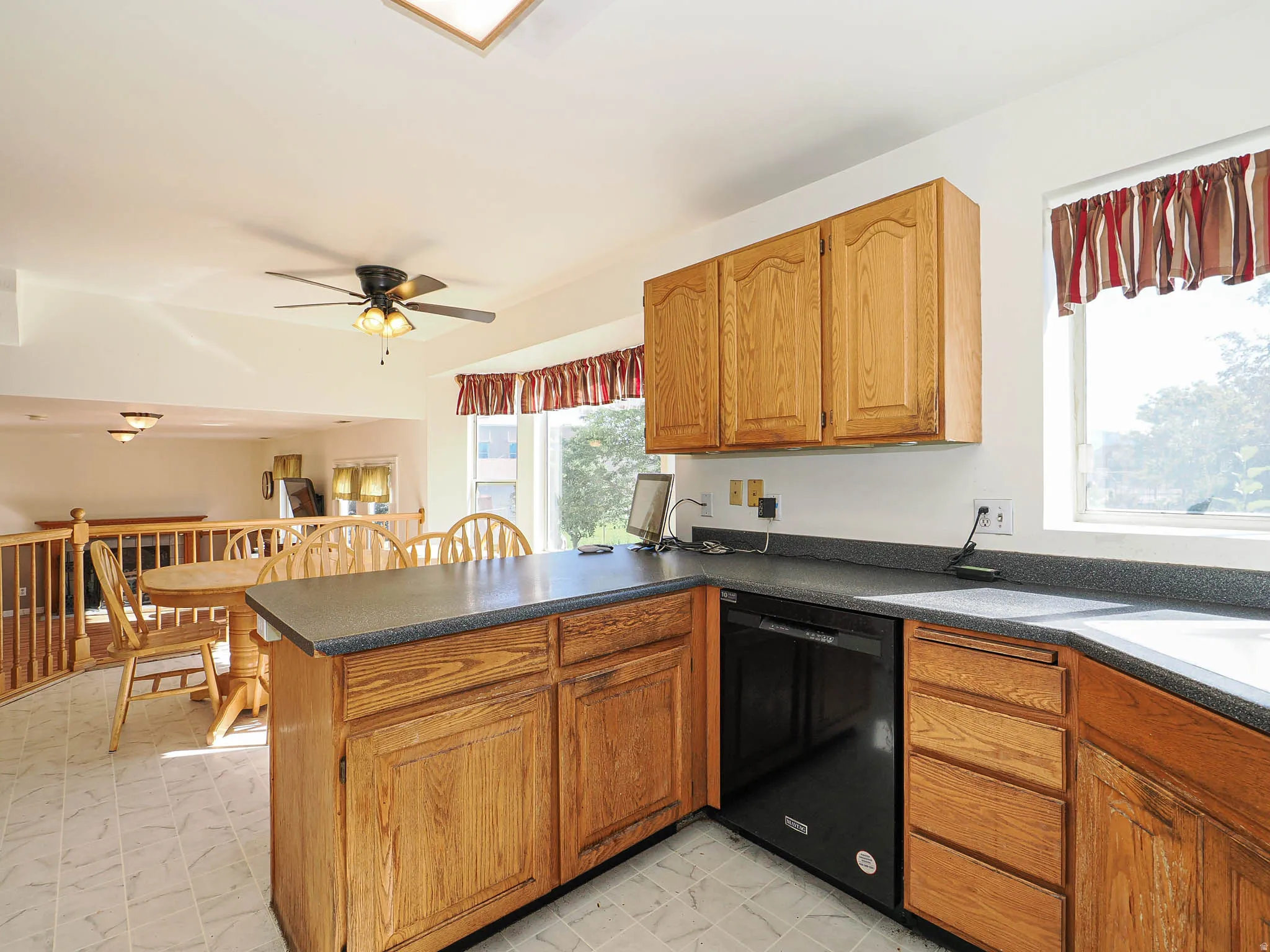 Kitchen featuring natural wood cabinetry, a built-in dishwasher, black countertops, and tile flooring