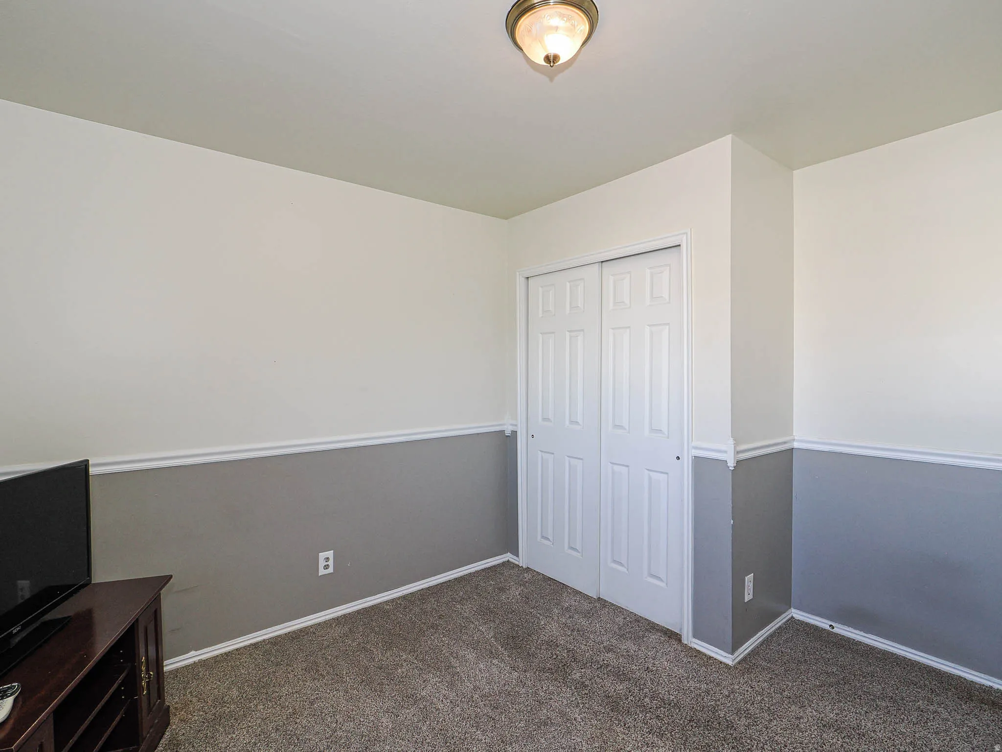 Room featuring white walls above a gray wainscoting, white baseboards, and neutral carpet