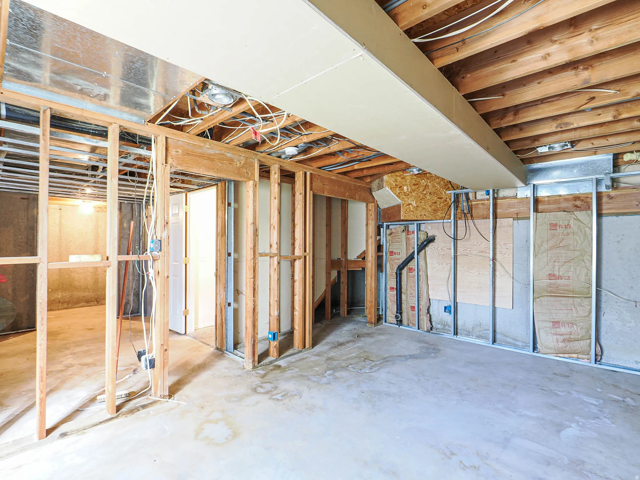 Unfinished basement space featuring visible wood framing, concrete flooring, exposed ceiling joists, and a partial dropped ceiling section
